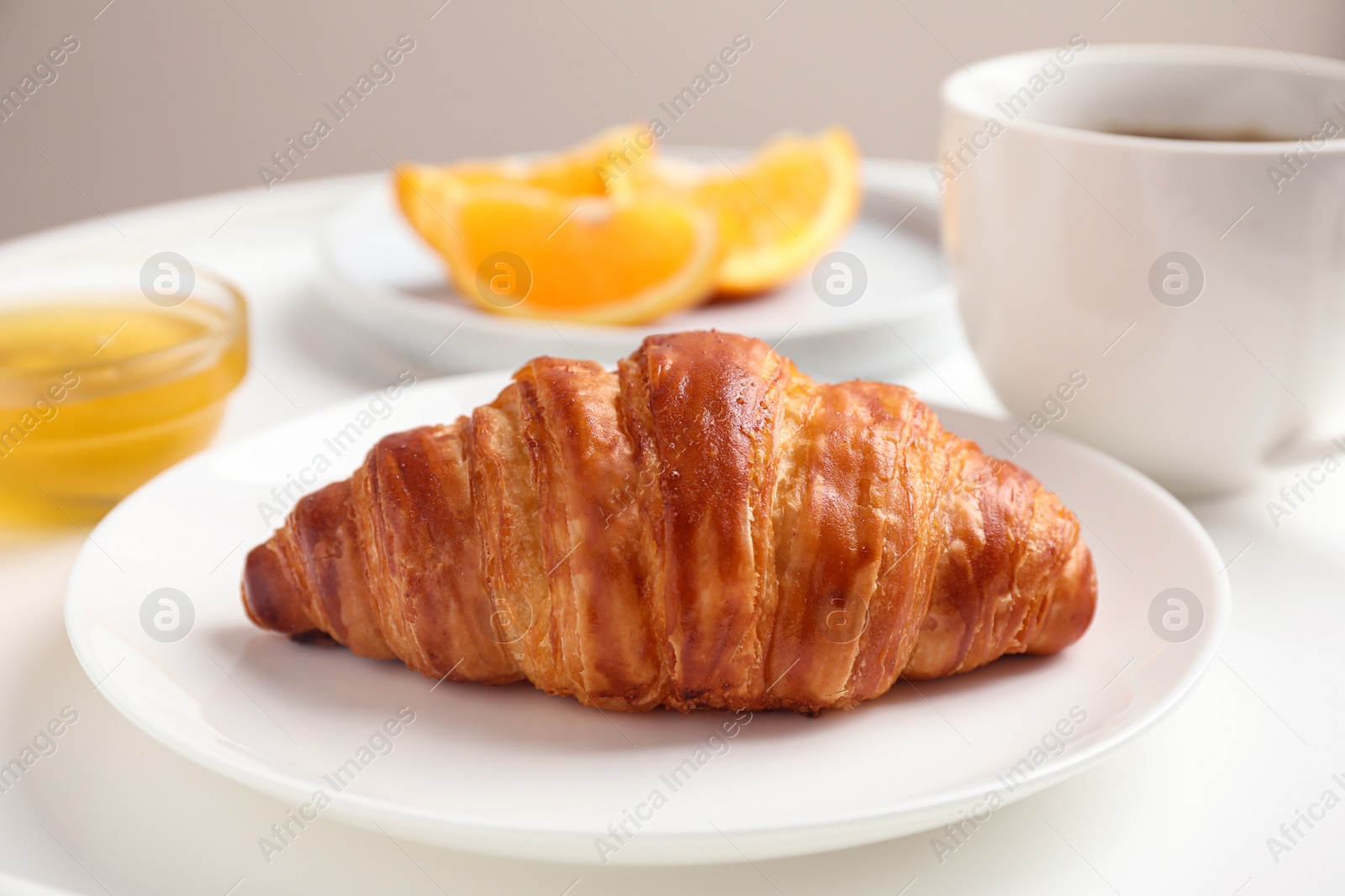 Photo of Delicious breakfast with croissant and honey on white table, closeup