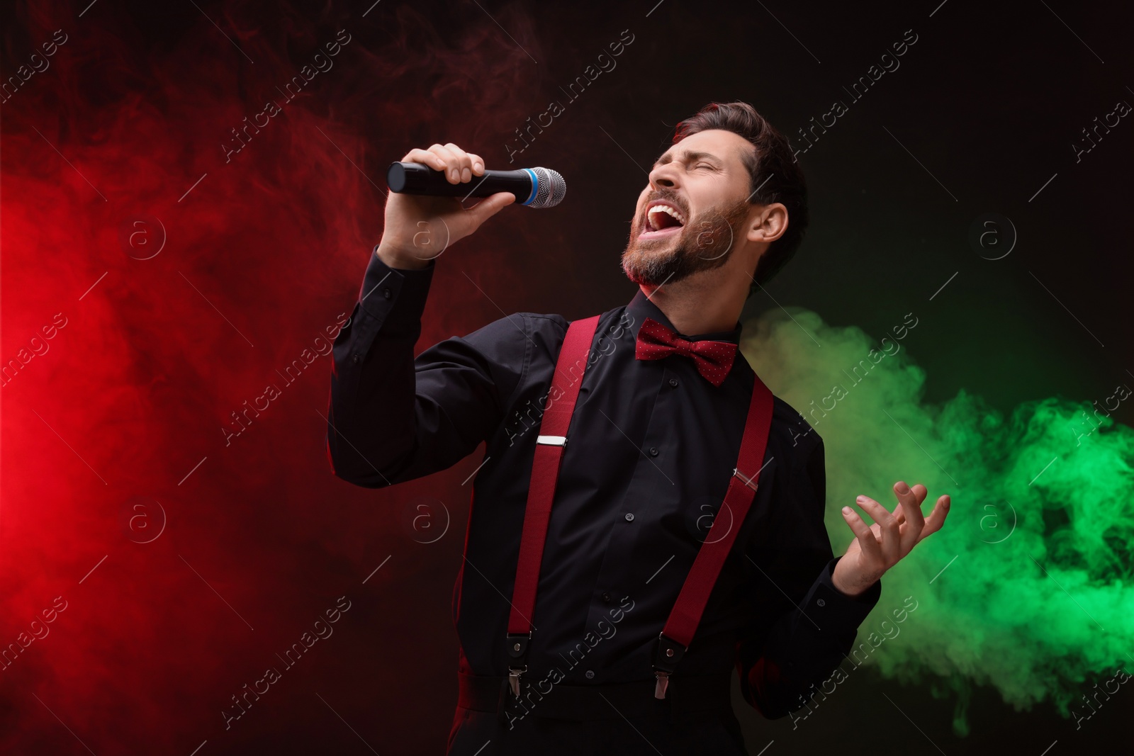 Photo of Emotional man with microphone singing in color lights. Space for text