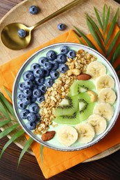 Photo of Tasty smoothie bowl with fresh fruits and oatmeal served on wooden table, top view