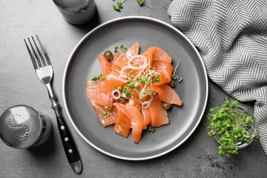 Photo of Salmon carpaccio with capers, onion and microgreens on grey table, flat lay