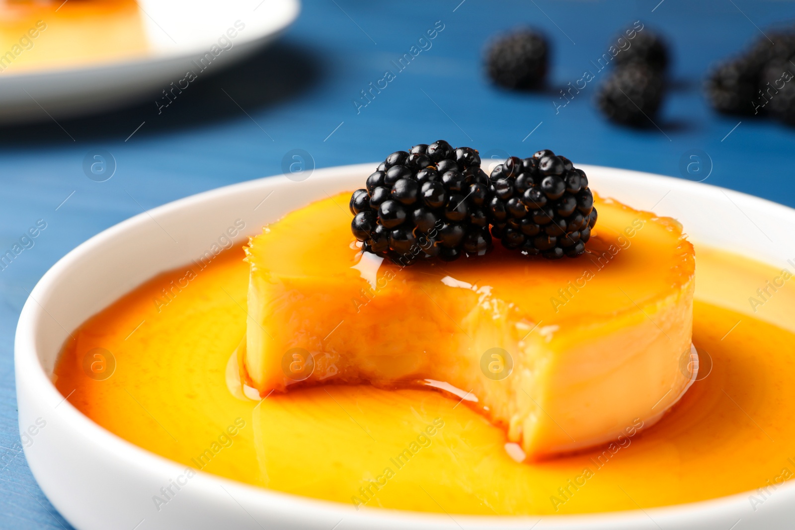 Photo of Delicious pudding with caramel and blackberries on blue wooden table, closeup