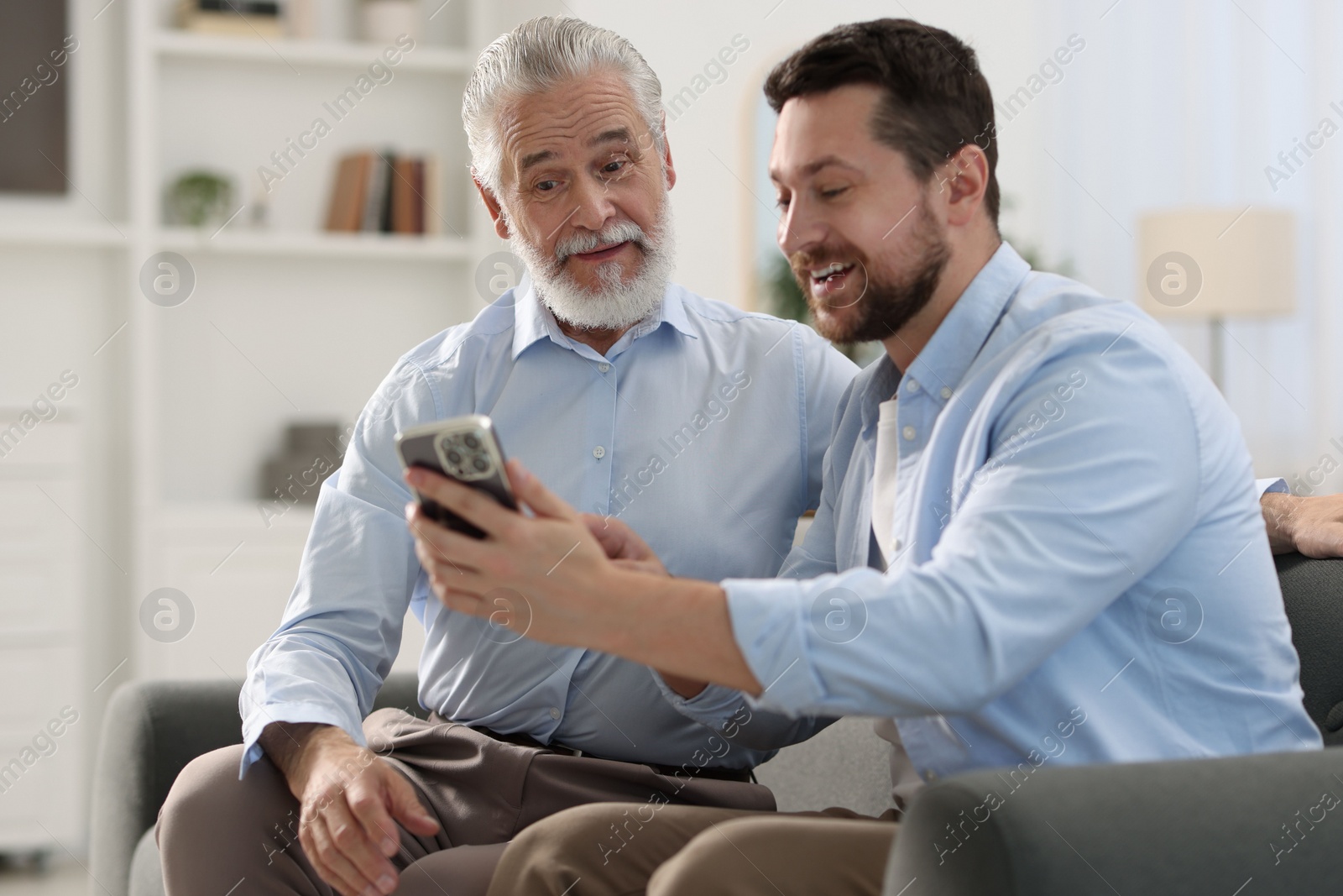 Photo of Happy son with smartphone and his dad on sofa at home