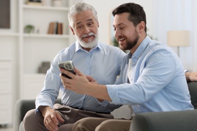 Happy son with smartphone and his dad on sofa at home