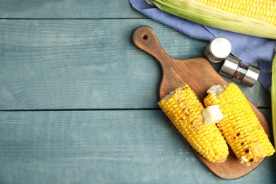 Photo of Fresh grilled corn cobs with butter on blue wooden table, flat lay. Space for text