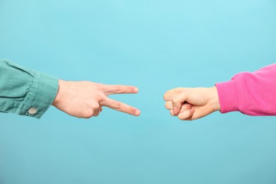 Photo of People playing rock, paper and scissors on light blue background, closeup