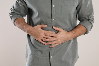 Photo of Man suffering from stomach ache on beige background, closeup. Food poisoning