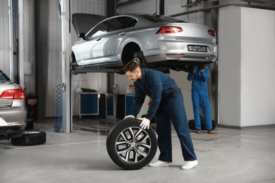 Technician with car wheel in automobile repair shop