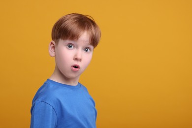 Photo of Portrait of surprised little boy on orange background, space for text