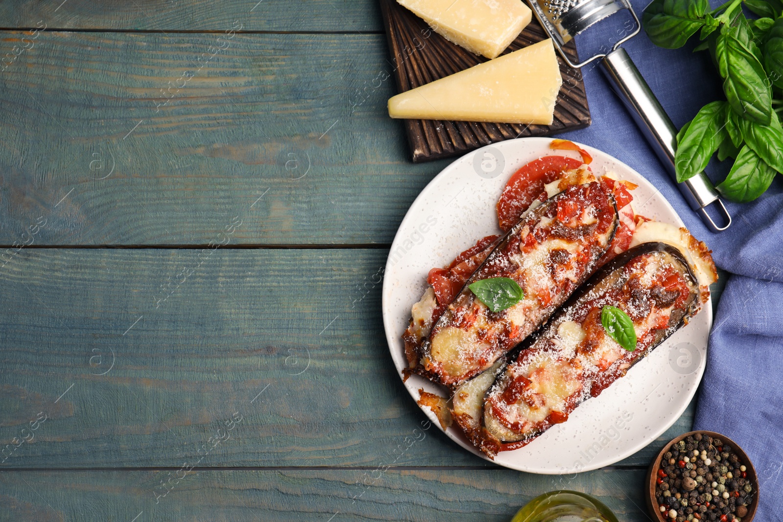 Photo of Baked eggplant with tomatoes, cheese and basil served on blue wooden table, flat lay. Space for text
