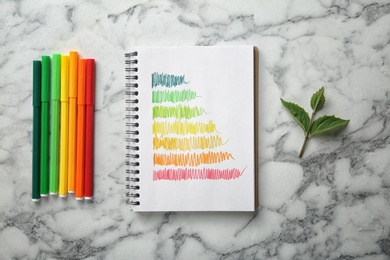 Photo of Notebook with colorful bars and markers on white marble background, flat lay. Energy efficiency rating chart