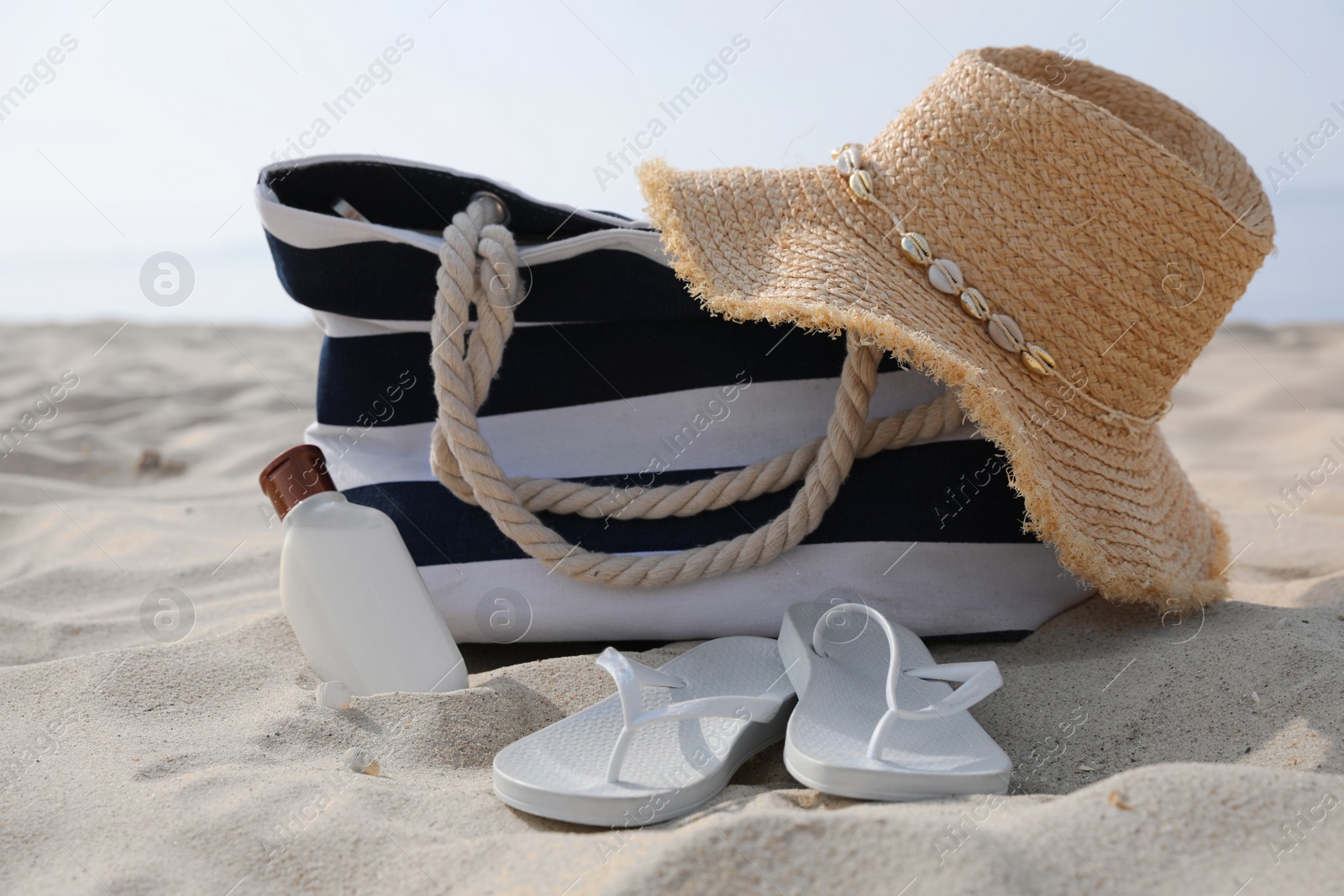 Photo of Beach bag, hat, sunscreen and flip flops on sandy seashore