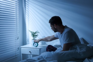 Sleepy man turning off alarm clock on nightstand in morning