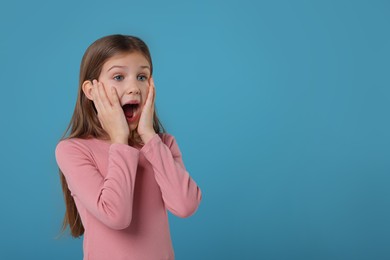 Portrait of surprised girl on light blue background. Space for text