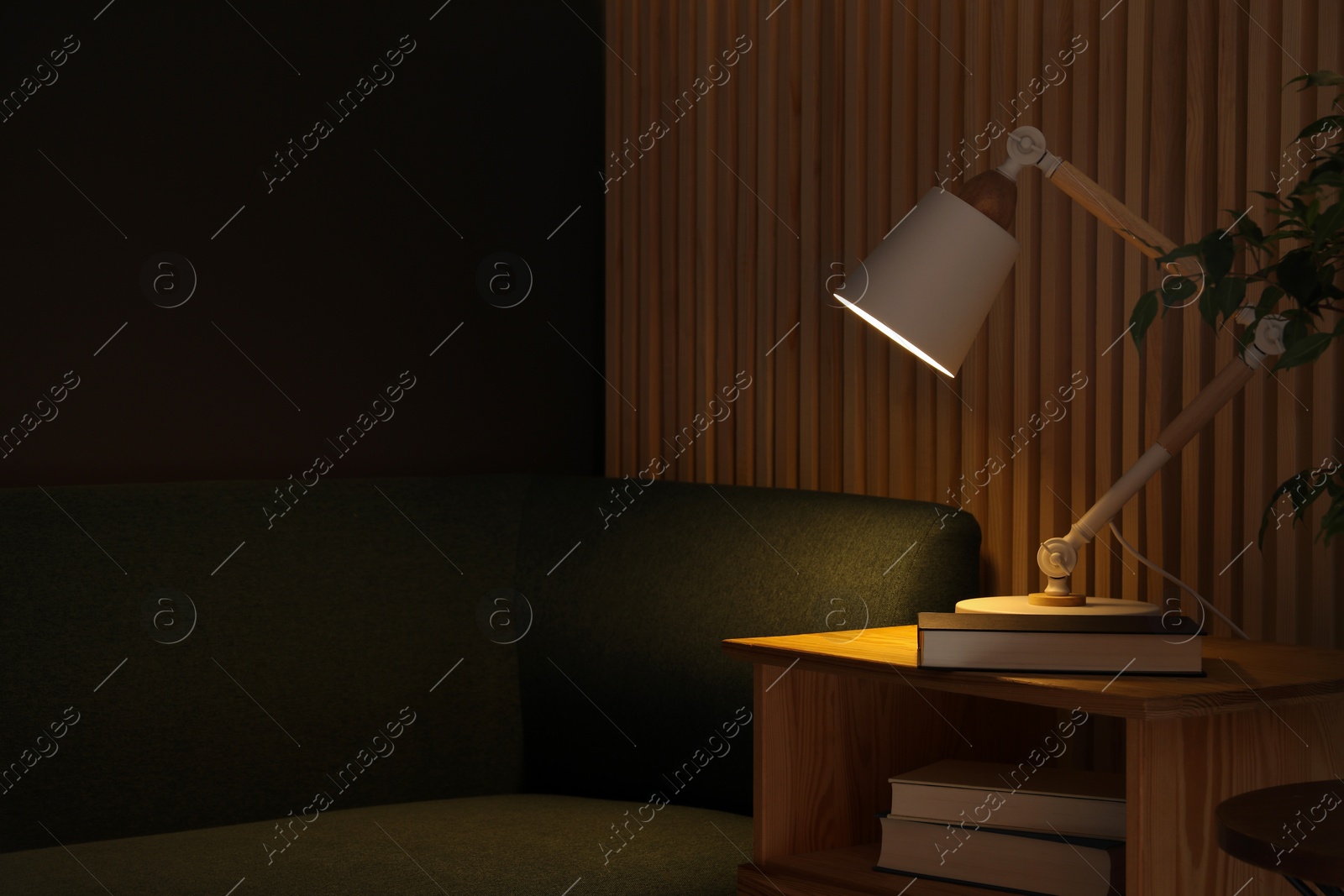 Photo of Stylish modern desk lamp and book on wooden cabinet in living room