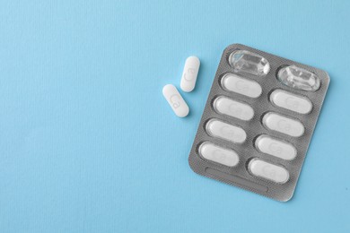 Photo of Blister pack with calcium supplement pills on light blue background, flat lay. Space for text