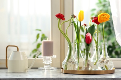 Photo of Different beautiful spring flowers in glassware, watering can and candle on window sill