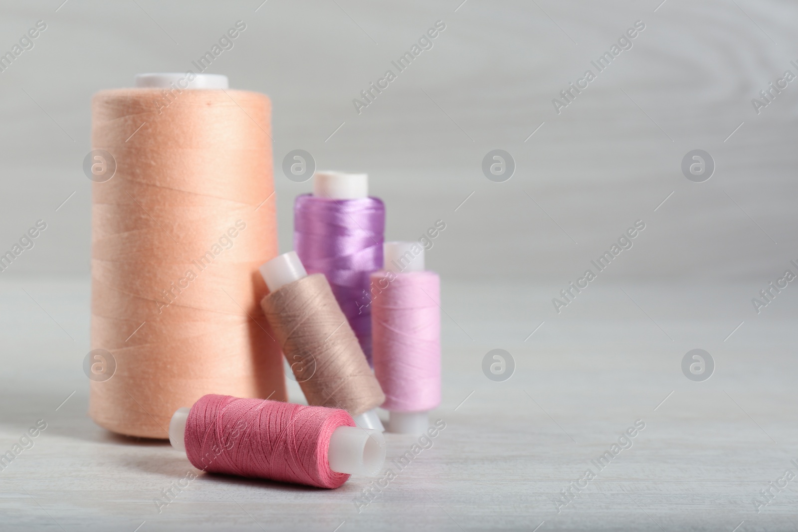 Photo of Group of color threads coils on white wooden table. Space for text