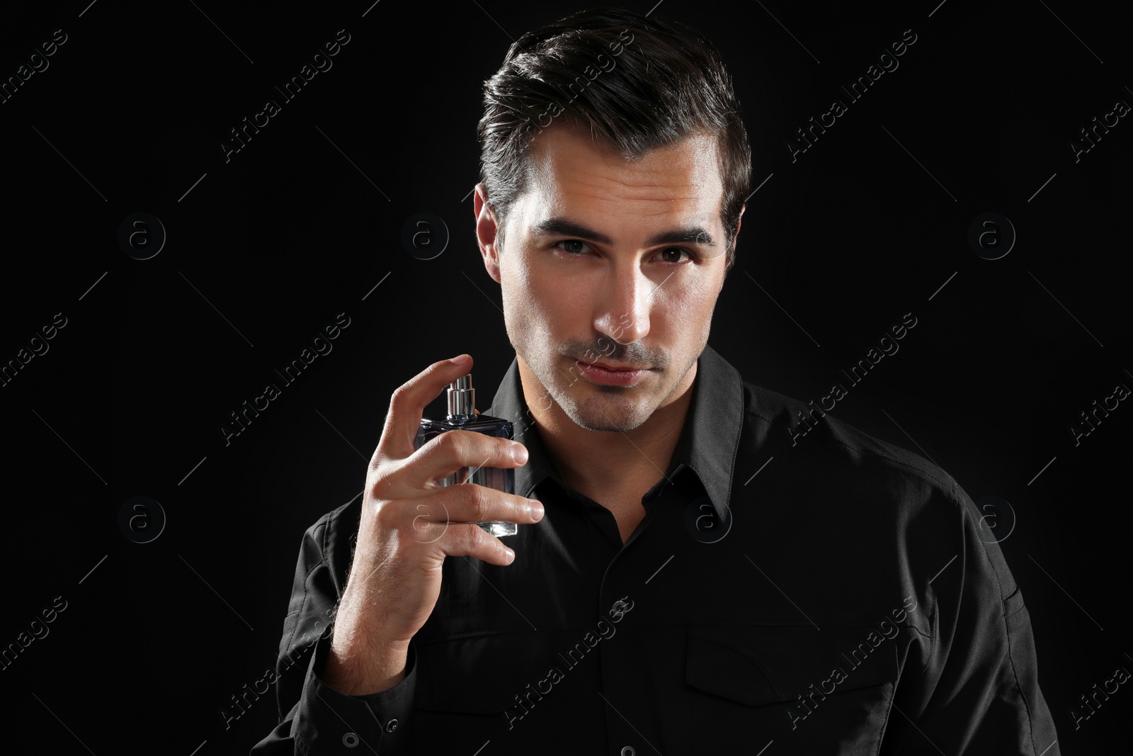 Photo of Handsome young man using perfume on black background