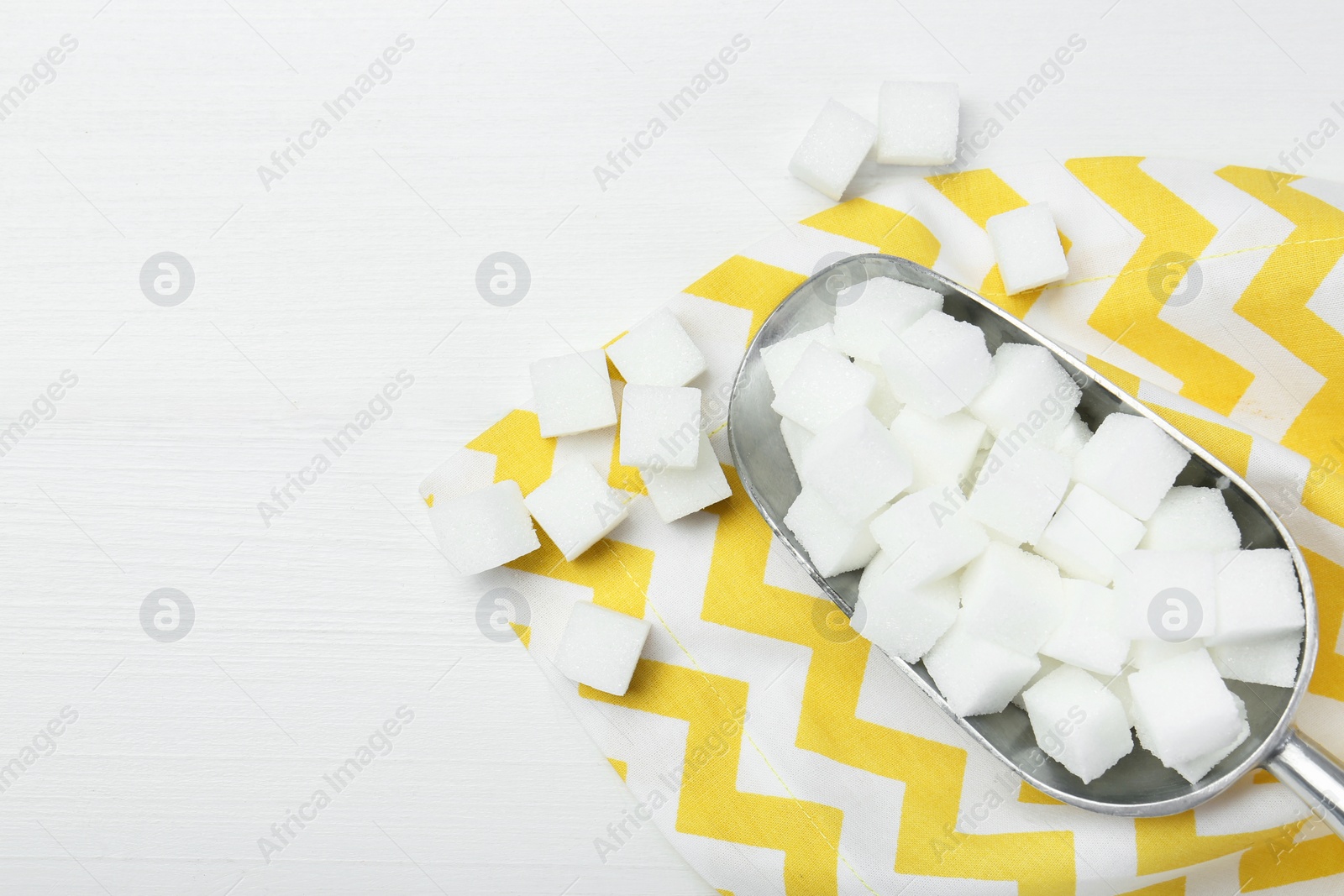 Photo of Many sugar cubes and metal scoop on white wooden table, top view. Space for text