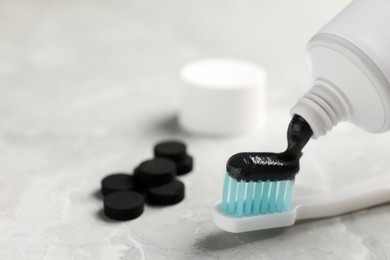 Photo of Applying charcoal toothpaste on brush on light grey table, closeup. Space for text