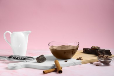 Bowl with tasty melted chocolate, pieces and cinnamon sticks on pink marble table