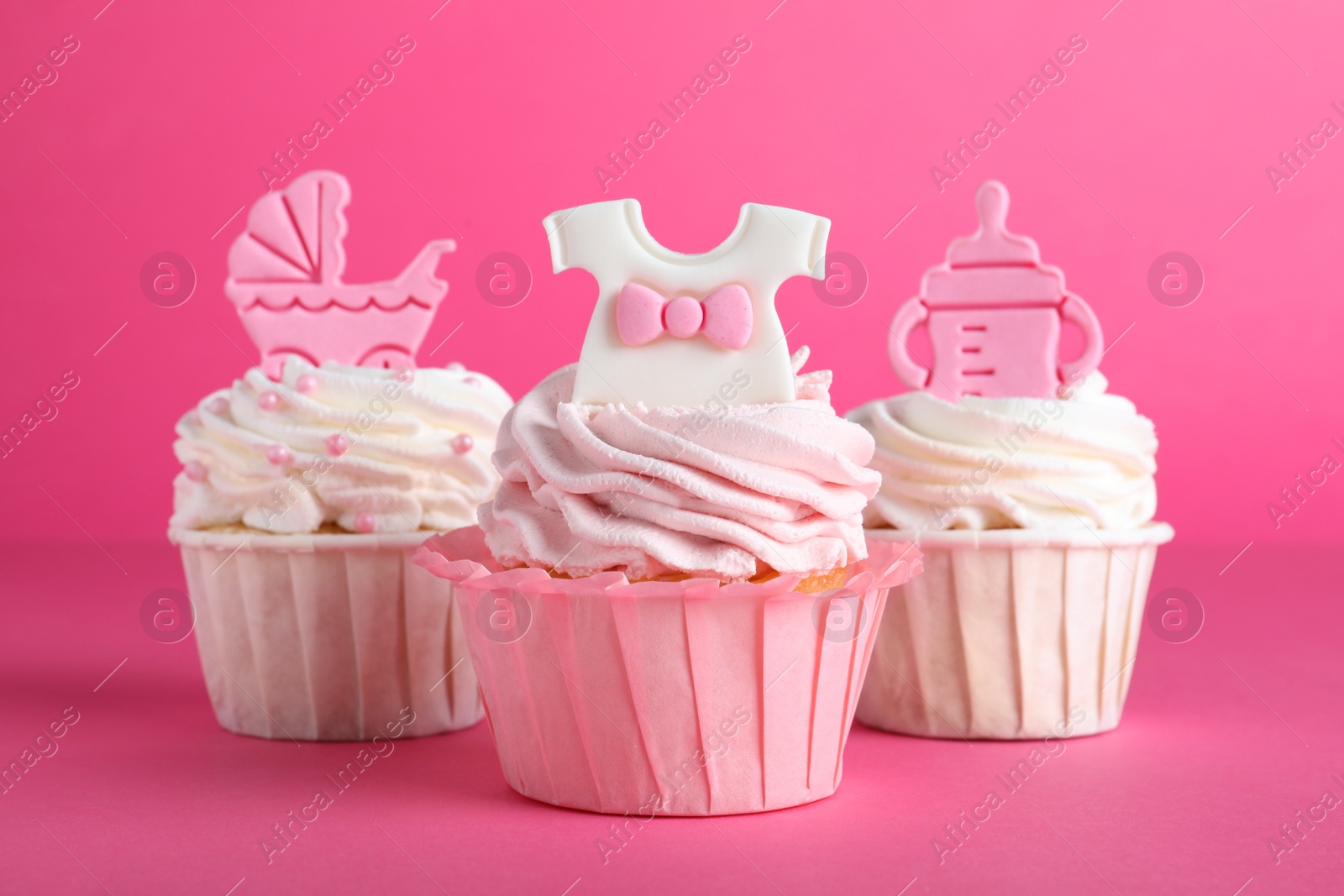 Photo of Beautifully decorated baby shower cupcakes for girl with cream and toppers on pink background