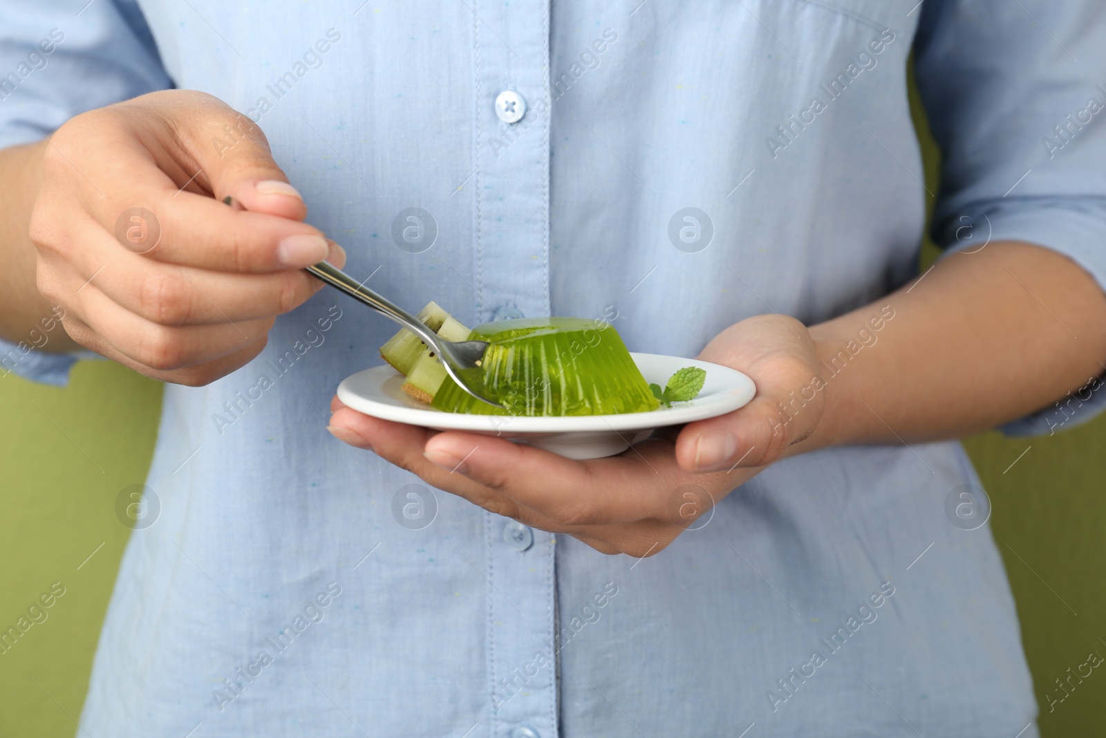 Photo of Young woman eating tasty kiwi jelly on green background, closeup