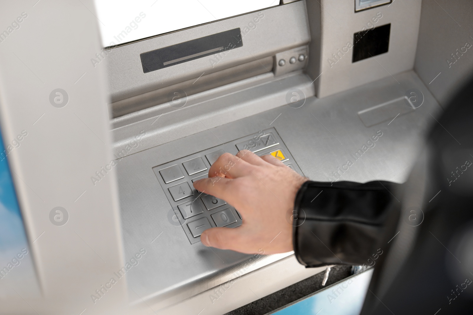 Photo of Man entering PIN code on cash machine keypad outdoors, closeup view