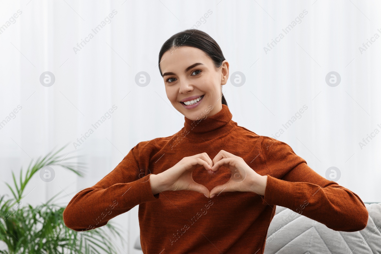 Photo of Happy young woman making heart with hands at home