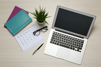 Modern laptop, glasses and office stationery on white wooden table, flat lay. Distance learning