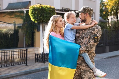 Soldier in military uniform reunited with his family and Ukrainian flag on city street, space for text