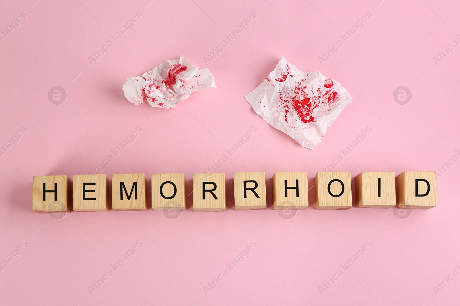 Photo of Wooden cubes with word HEMORRHOID and toilet paper on pink background, flat lay