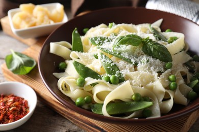 Photo of Delicious pasta with green peas, fresh basil and cheese on wooden table, closeup