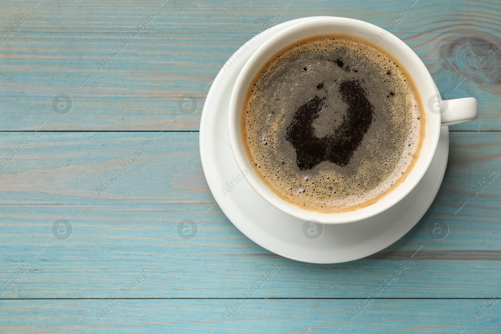 Photo of Cup of aromatic coffee on light blue wooden table, top view. Space for text