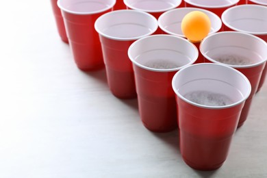 Photo of Plastic cups and ball on white table, space for text. Beer pong game