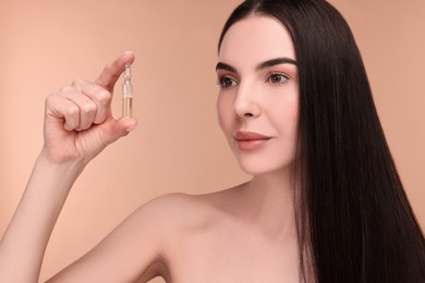 Beautiful young woman holding skincare ampoule on beige background