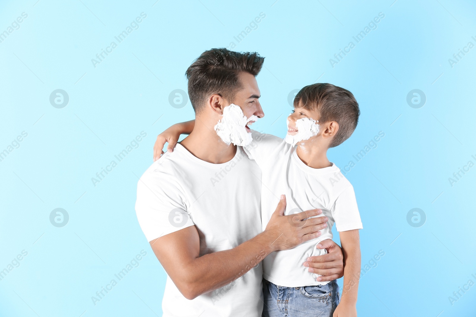 Photo of Father and son with shaving foam on faces against color background