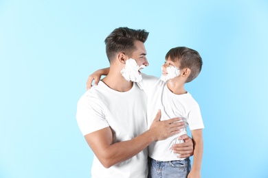 Father and son with shaving foam on faces against color background