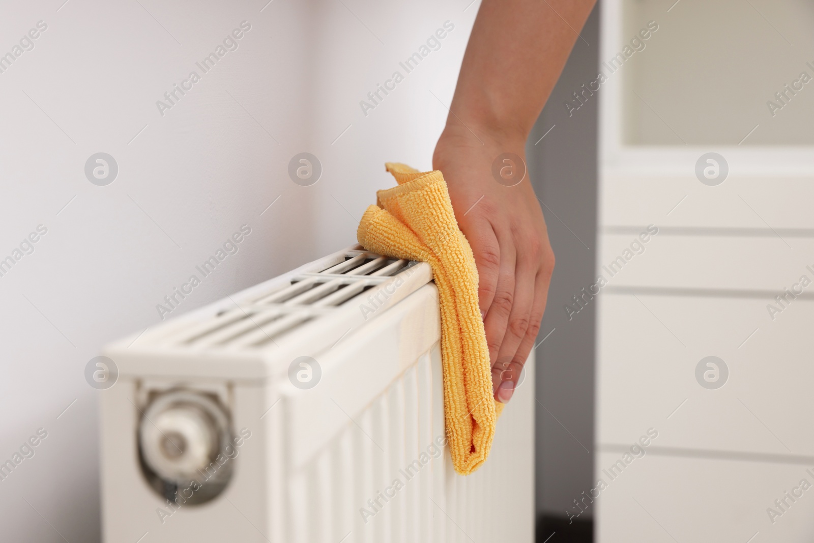 Photo of Woman cleaning radiator with rag indoors, closeup