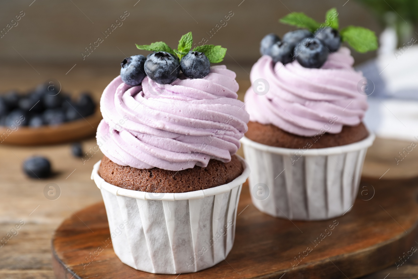 Photo of Sweet cupcakes with fresh blueberries on wooden board, closeup