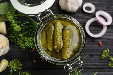 Photo of Glass jar of pickled cucumbers on black wooden table, flat lay