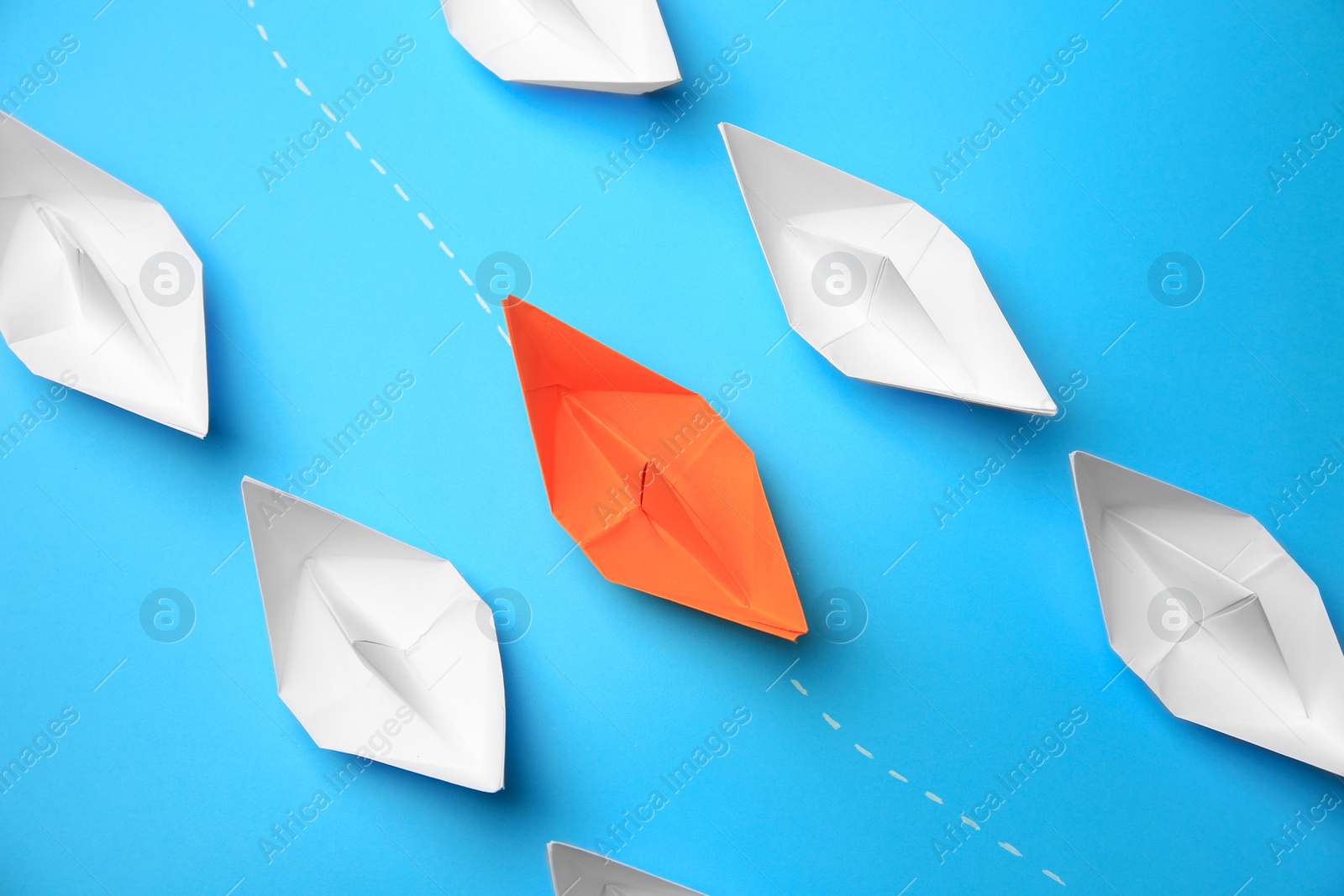 Photo of Orange paper boat floating between others on light blue background, flat lay. Uniqueness concept