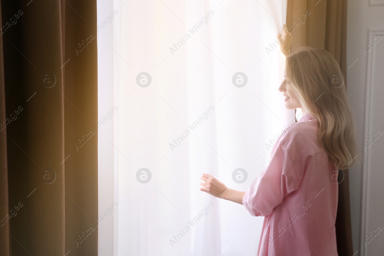 Photo of Young woman opening window curtains at home