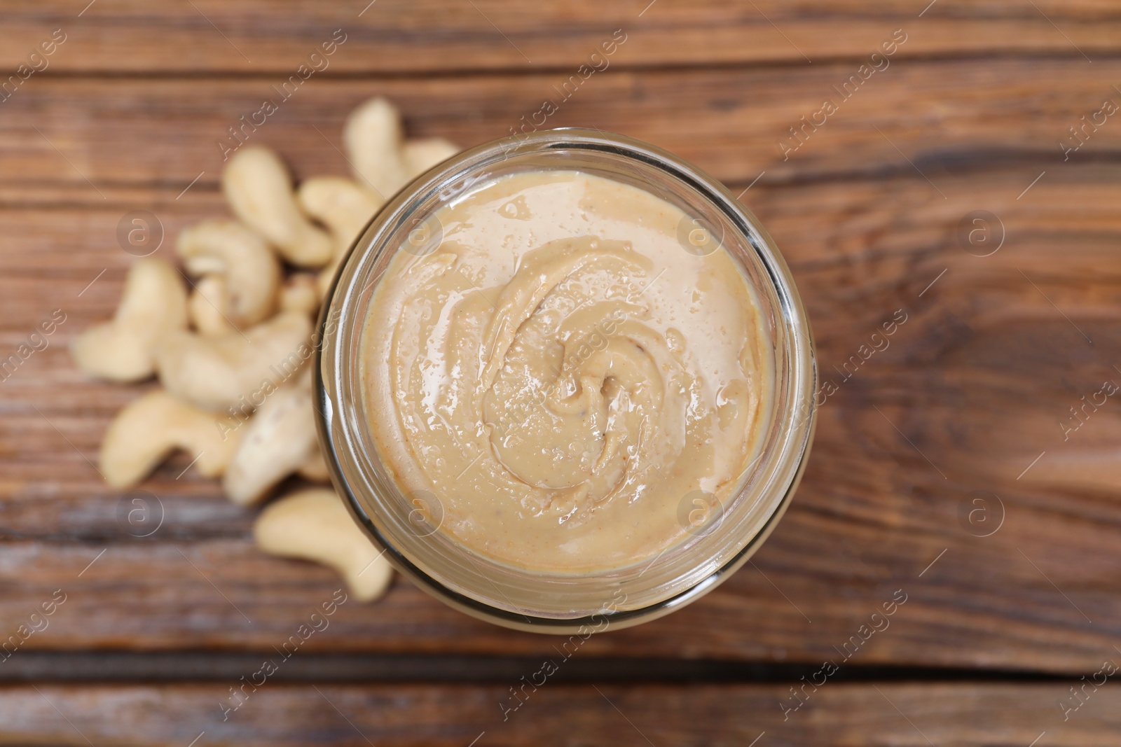 Photo of Tasty cashew nut paste in jar on wooden table, top view