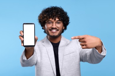 Handsome smiling man showing smartphone on light blue background, selective focus