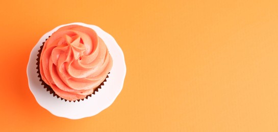 Photo of Delicious cupcake with bright cream on orange background, top view. Space for text