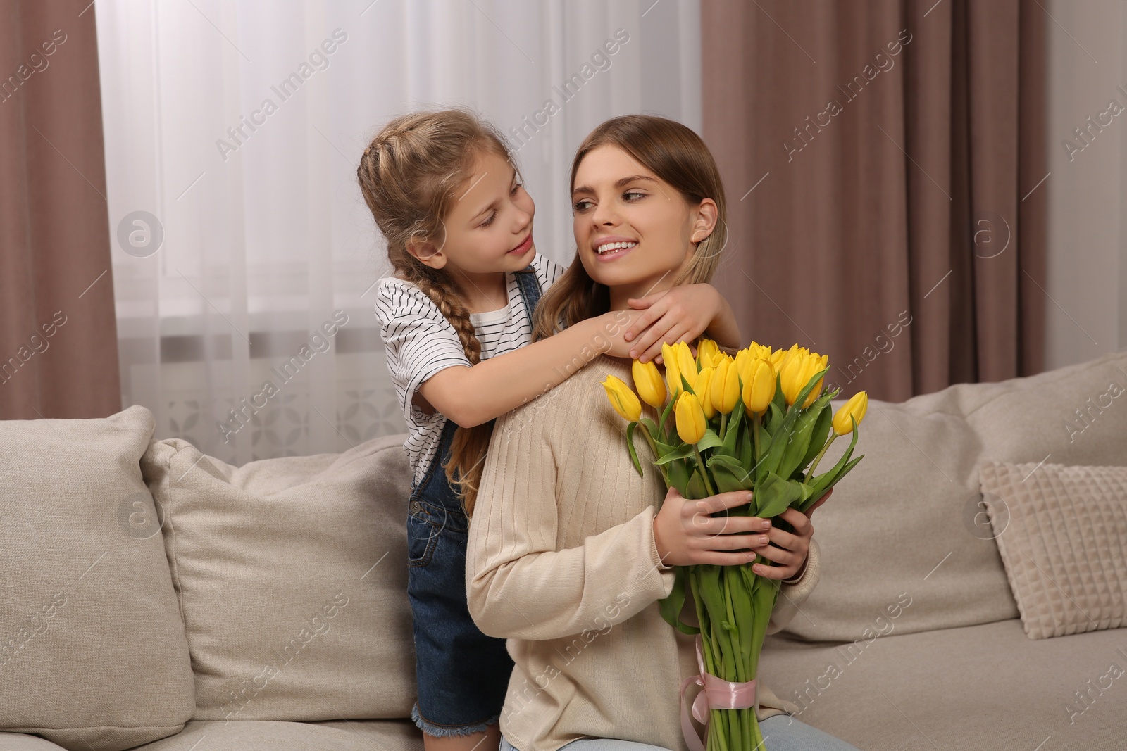 Photo of Little daughter congratulating mom with bouquet of yellow tulips at home. Happy Mother's Day