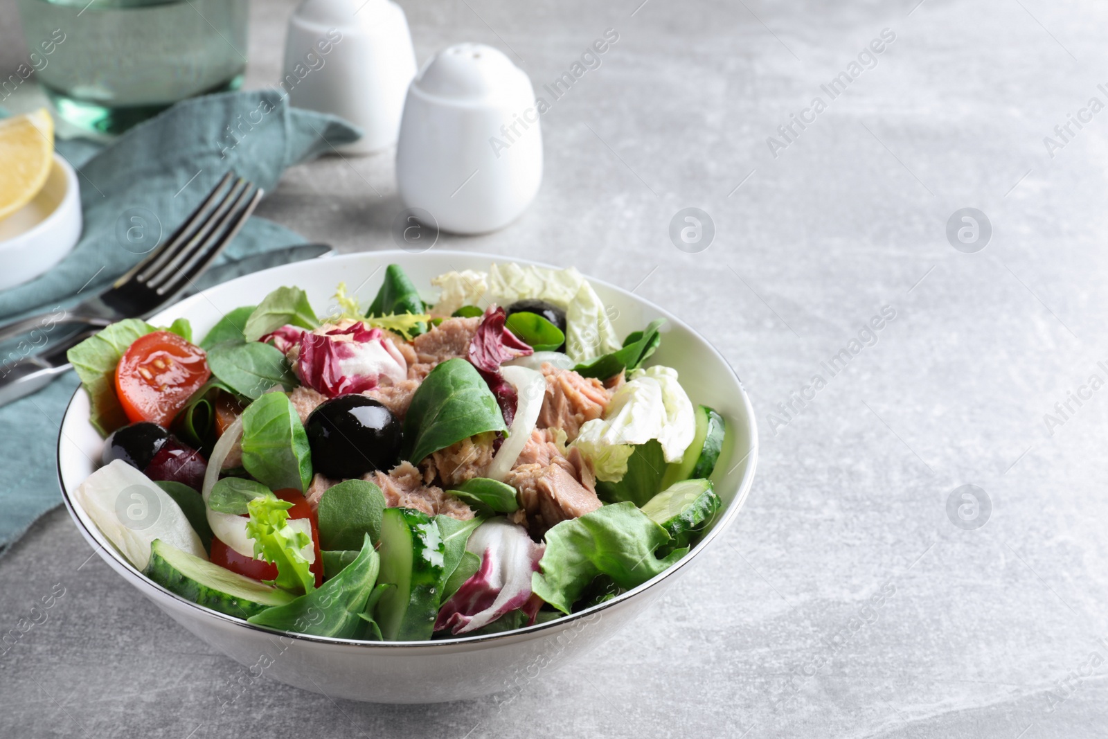 Photo of Bowl of delicious salad with canned tuna and vegetables on light grey table, space for text