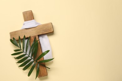 Wooden cross, white cloth and palm leaf on beige background, top view with space for text. Easter attributes