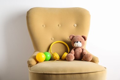 Photo of Baby songs. Toy bear, headphones and balls on armchair near white wall